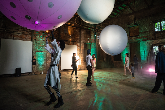 People in an old warehouse, batting large colorful balloons around