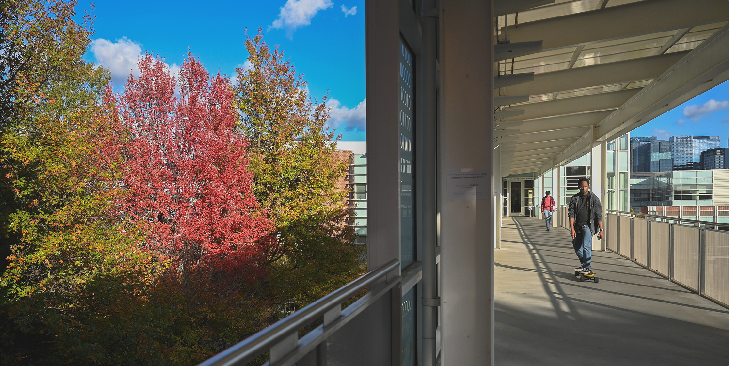A student skateboards across the library bridge