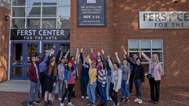 Students standing with one hand raised outside of the Ferst Center for the Arts.