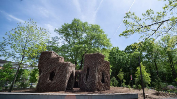 Image of Stickworks sculpture by Patrick Dougherty entitled "A Chip off the Ol' Block". As was the original intent of this natural, woven fortress constructed in 2020, it has succumbed to the elements and will be responsibly and sustainably removed from its location in the EcoCommons in the fall of 2023.
