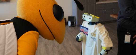 Photo of Buzz the mascot leaning down toward a small humanoid robot wearing a Georgia Tech t-shirt