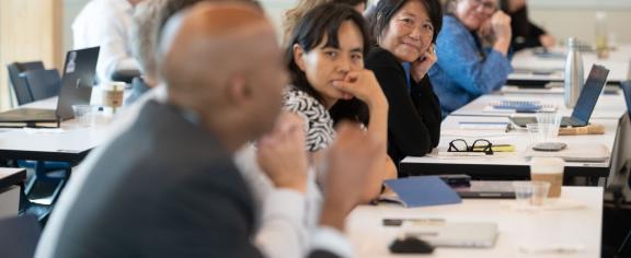 A group of faculty leaders are pictured together for a workshop, seating in a row at a long table. The camera is focused on Julie Kim, who is a member of a past cohort of ACC ALN Fellows.
