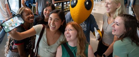 students taking a photo selfie with mascot Buzz.