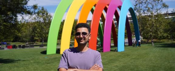 Man standing outside in front of rainbow sculpture 