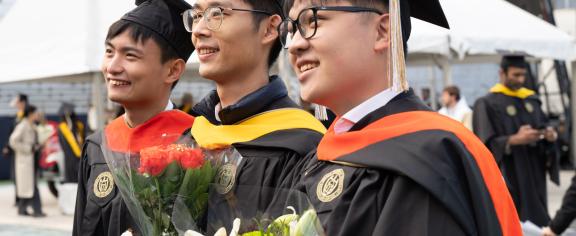 Group of three Georgia Tech students at commencement ceremony with flowers.