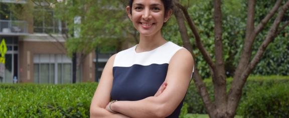 Farzaneh Najafi standing outside smiling with her arms crossed. Green foliage is visible in the background.