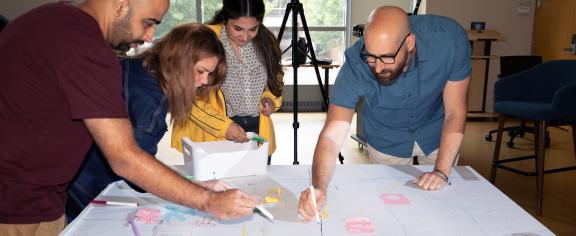 Attendees at the Spatial Scholarship Field School lean over a large table workspace marking up a map.